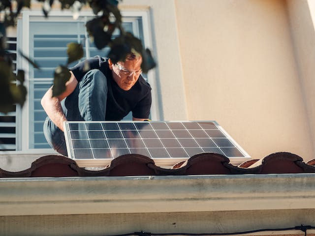 A man installs solar panels on a house roof