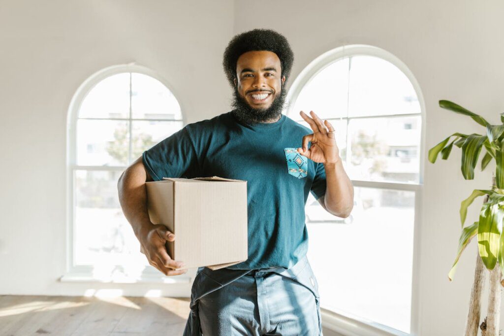 A man holding a cardboard box while looking at a camera and smiling