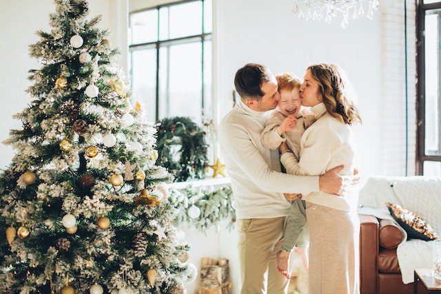 Mother and father holding their sun while standing next to a decorated Christmas tree in their home 