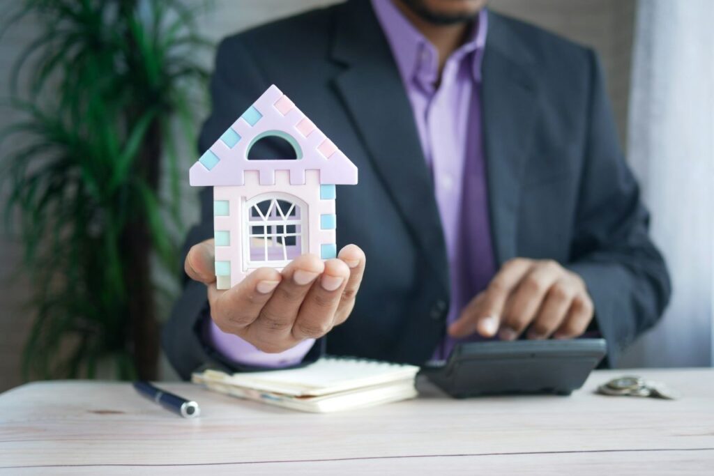 Man using a calculator while holding a miniature house.